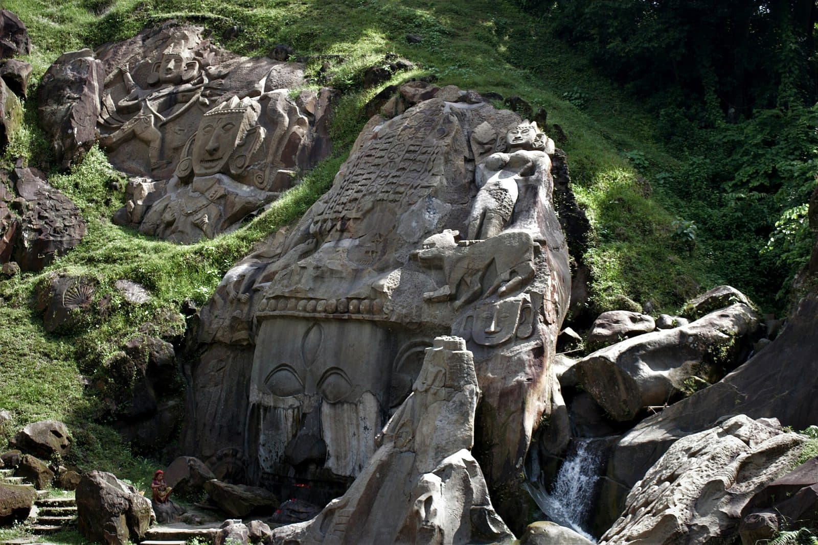 Large rock-cut faces and figures carved into a mossy hillside at Unakoti
